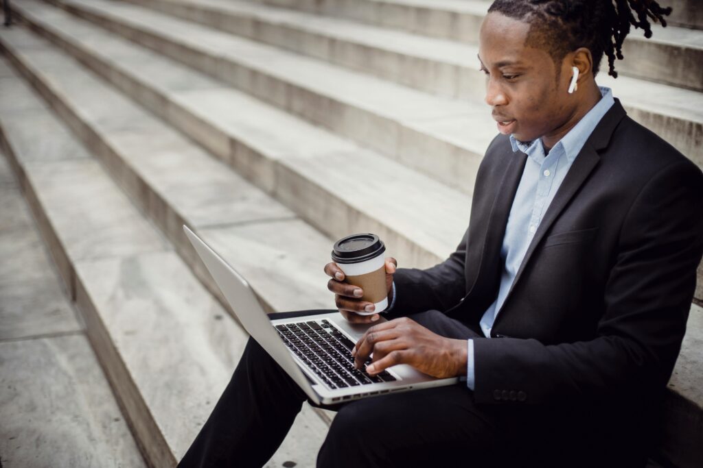 A young black man working on his laptop on a building steps.